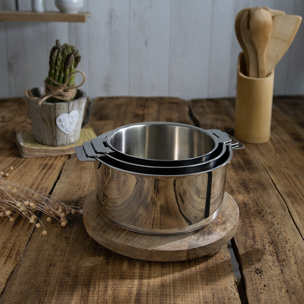 Set de 3 casseroles en inox brillant Du Bruit dans la Cuisine Mutine Cristel empilables sur une table en bois
